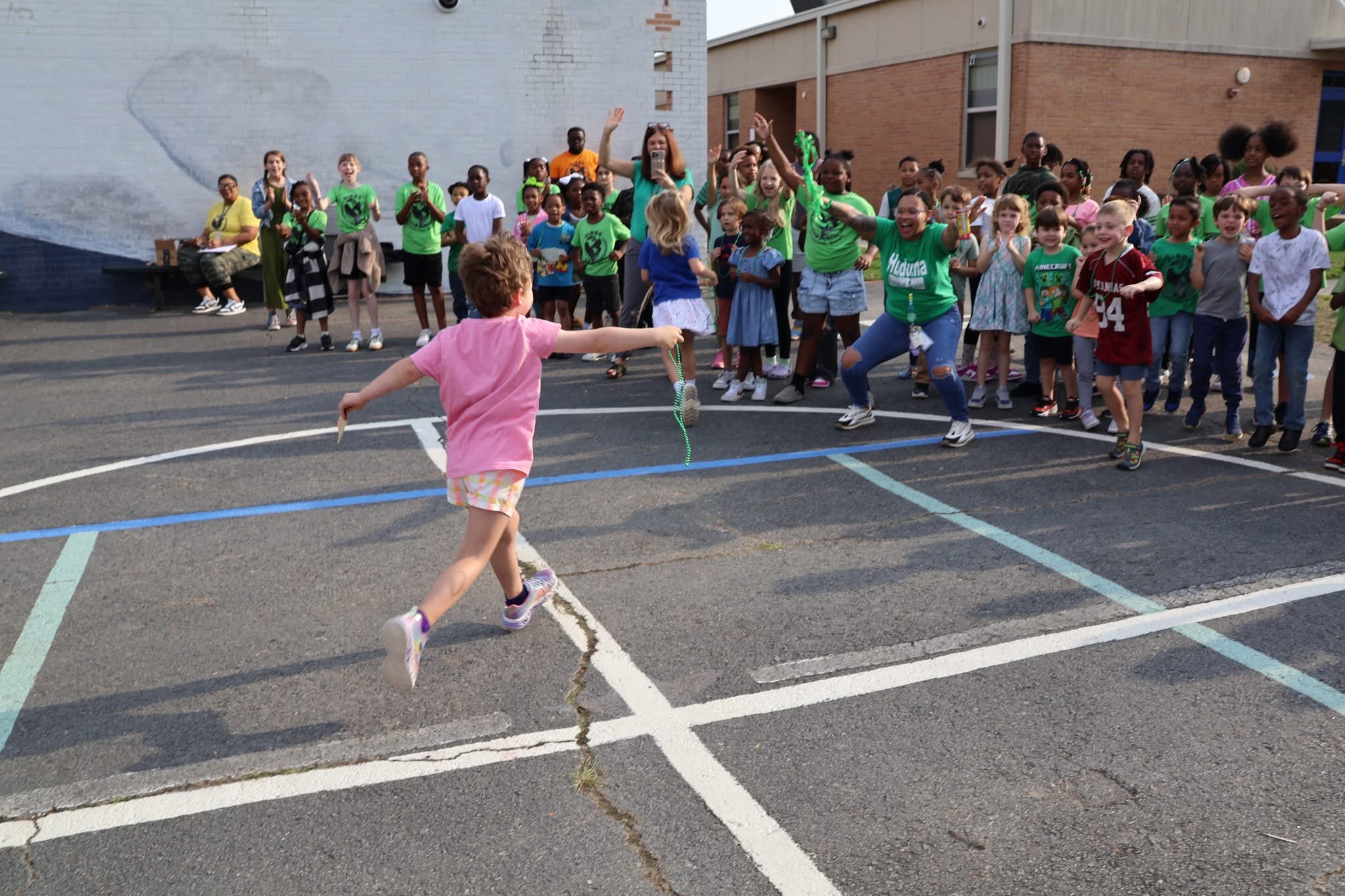 Gibbs students in green Huduma house shirts cheering during a playground relay race.